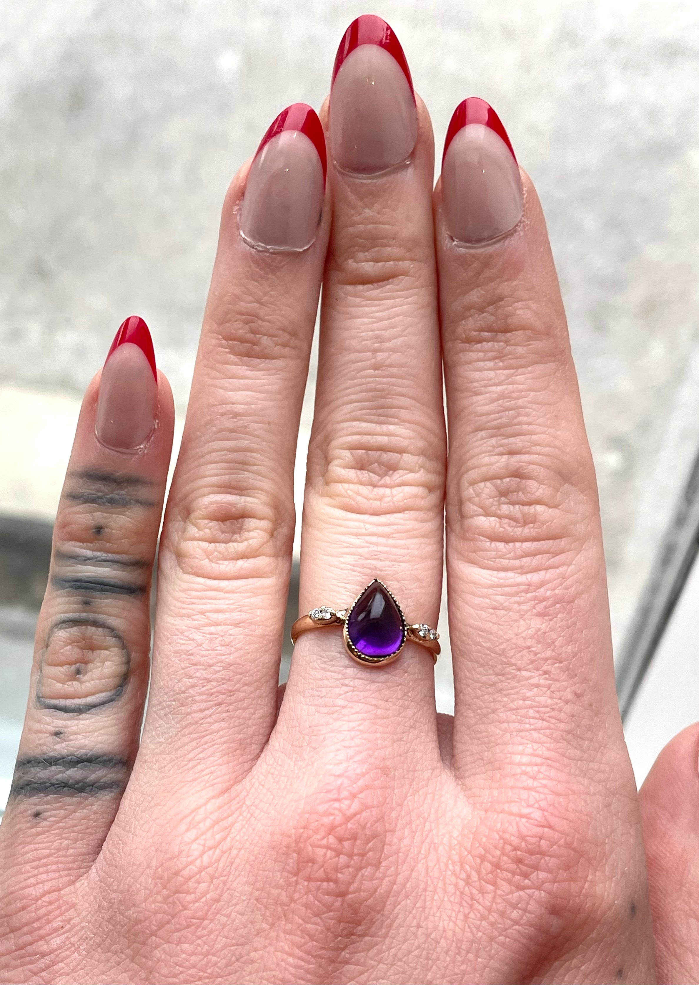 Antique ring. Pear shaped amethyst cabochon ring with four accent diamonds set into a tall shoulder setting. 14k yellow gold band and bezel with milgrain detailing. Worn on hand
pear, pear ring, amethyst, amethyst ring, amethyst pear shape, antique, antique ring, 14k yellow gold ring, hand restored ring, amethyst and diamond ring