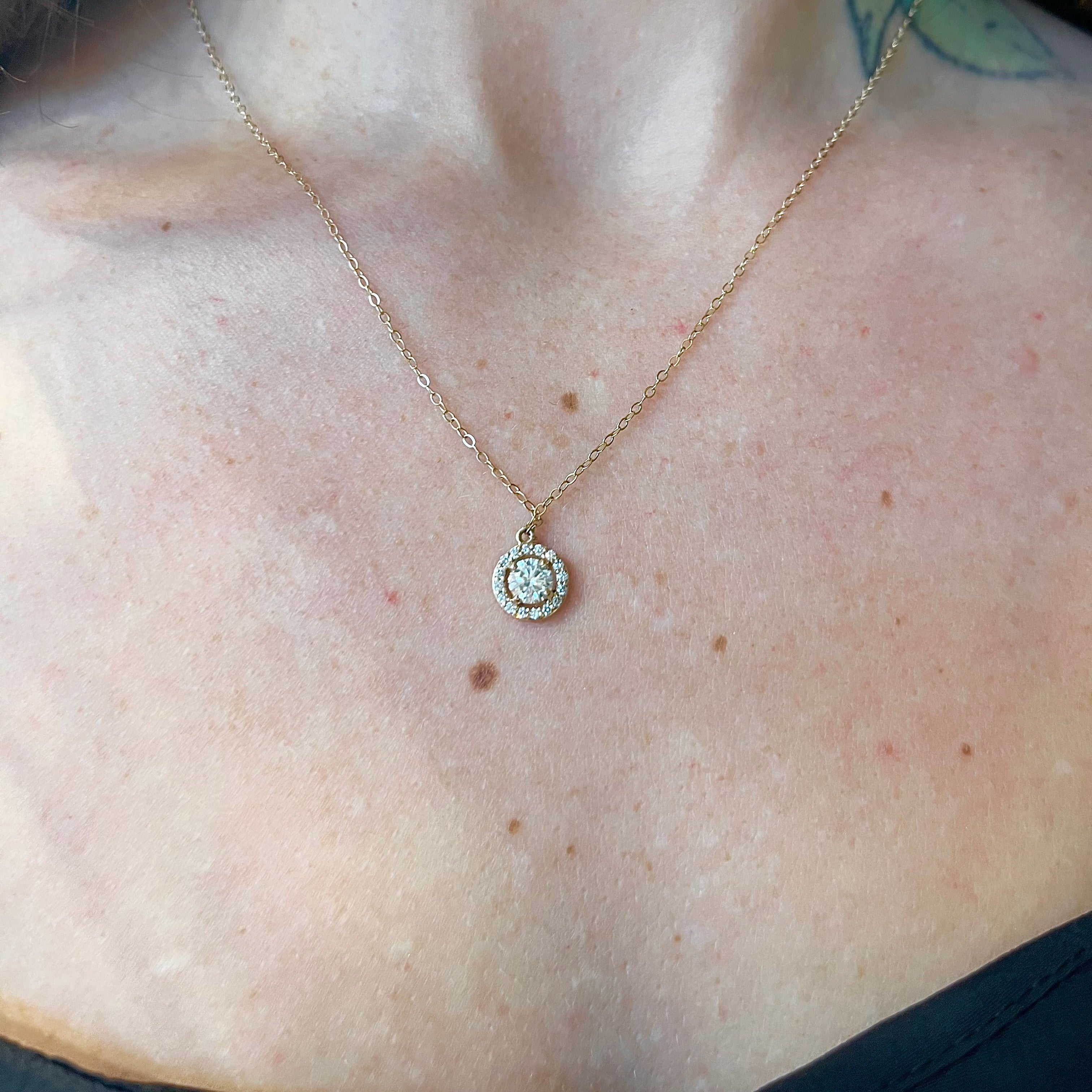 A 14k yellow gold diamond halo necklace with a round pendant design featuring a central diamond surrounded by a halo of smaller diamonds, attached to an 18-inch gold chain, antique and vintage, gold and diamond jewelry, 14k gold diamond necklace, halo diamond necklace, solid gold necklace, solid gold pendant, handmade jewelry, antique and vintage inspired, custom design, diamond halo necklace on a neck